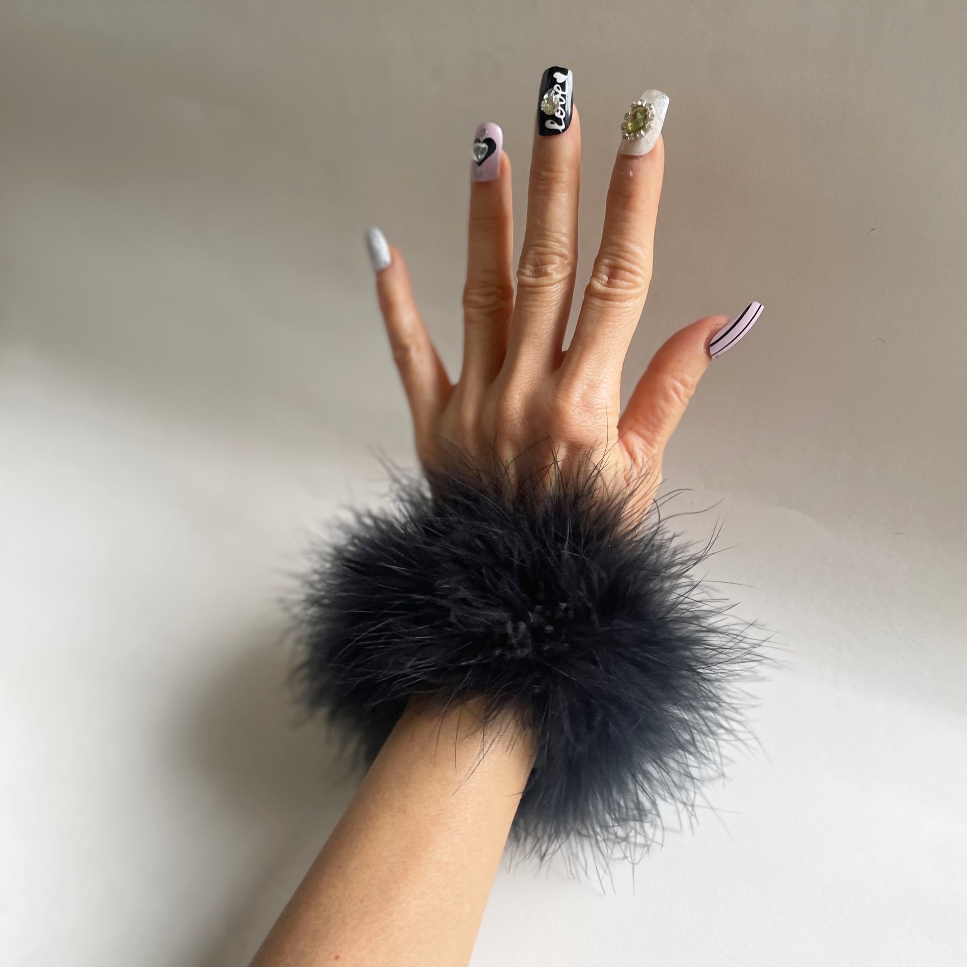 Hand wearing a black marabou feather cuff wrist accessory against a neutral background