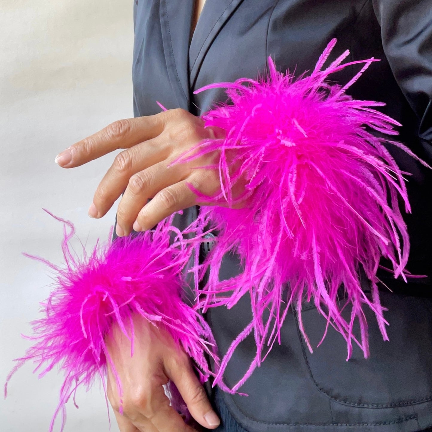 Person wearing a dark jacket wearing a pair of hot pink feather cuffs against a neutral background