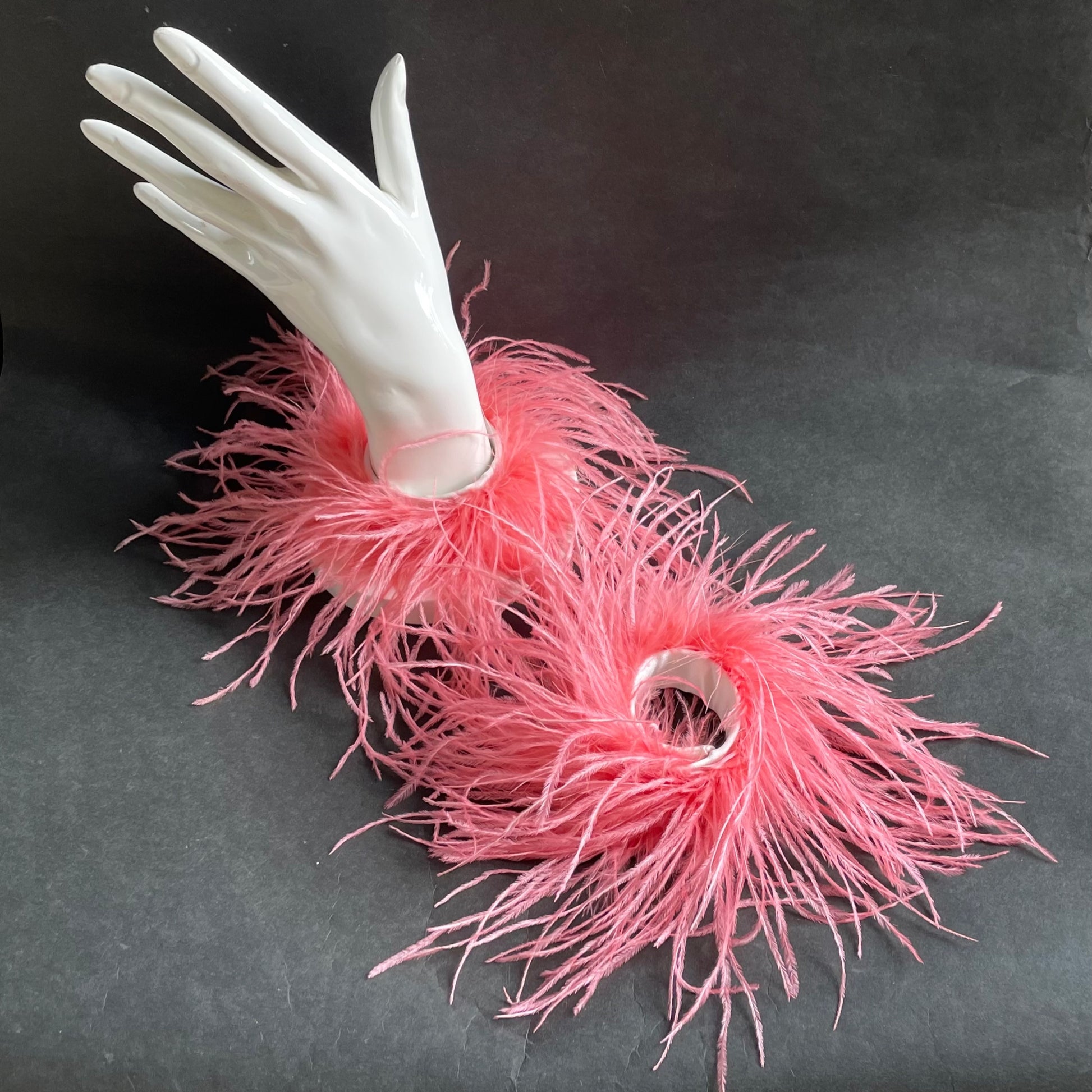 A set of pink feather cuff bracelets on a white mannequin hand against a dark background