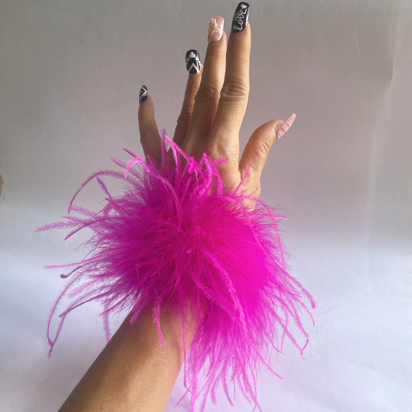 Hand wearing a hot pink feather cuff accessory against a plain background