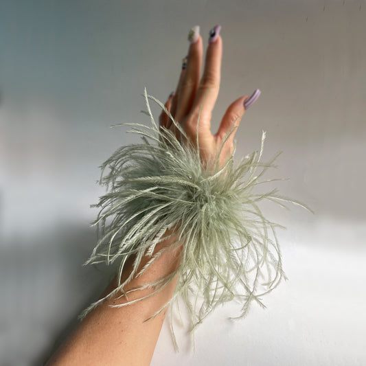 Hand wearing an olive green ostrich feather cuff against a neutral background