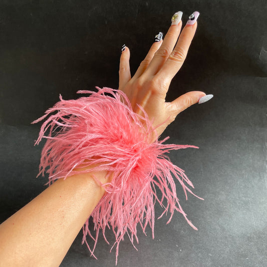 Hand wearing a pink feather cuff wrist accessory on a dark background