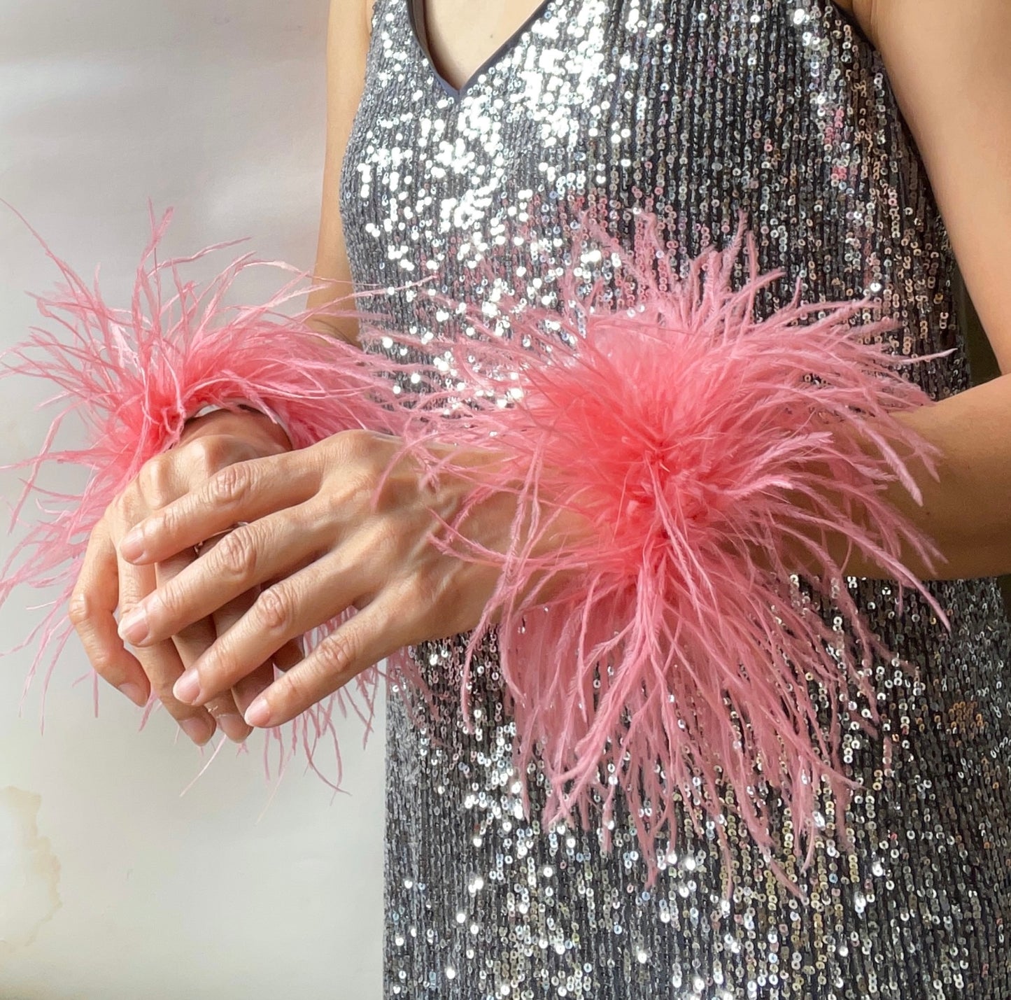 Person wearing a silver sequin dress with pink feather cuffs on a plain background