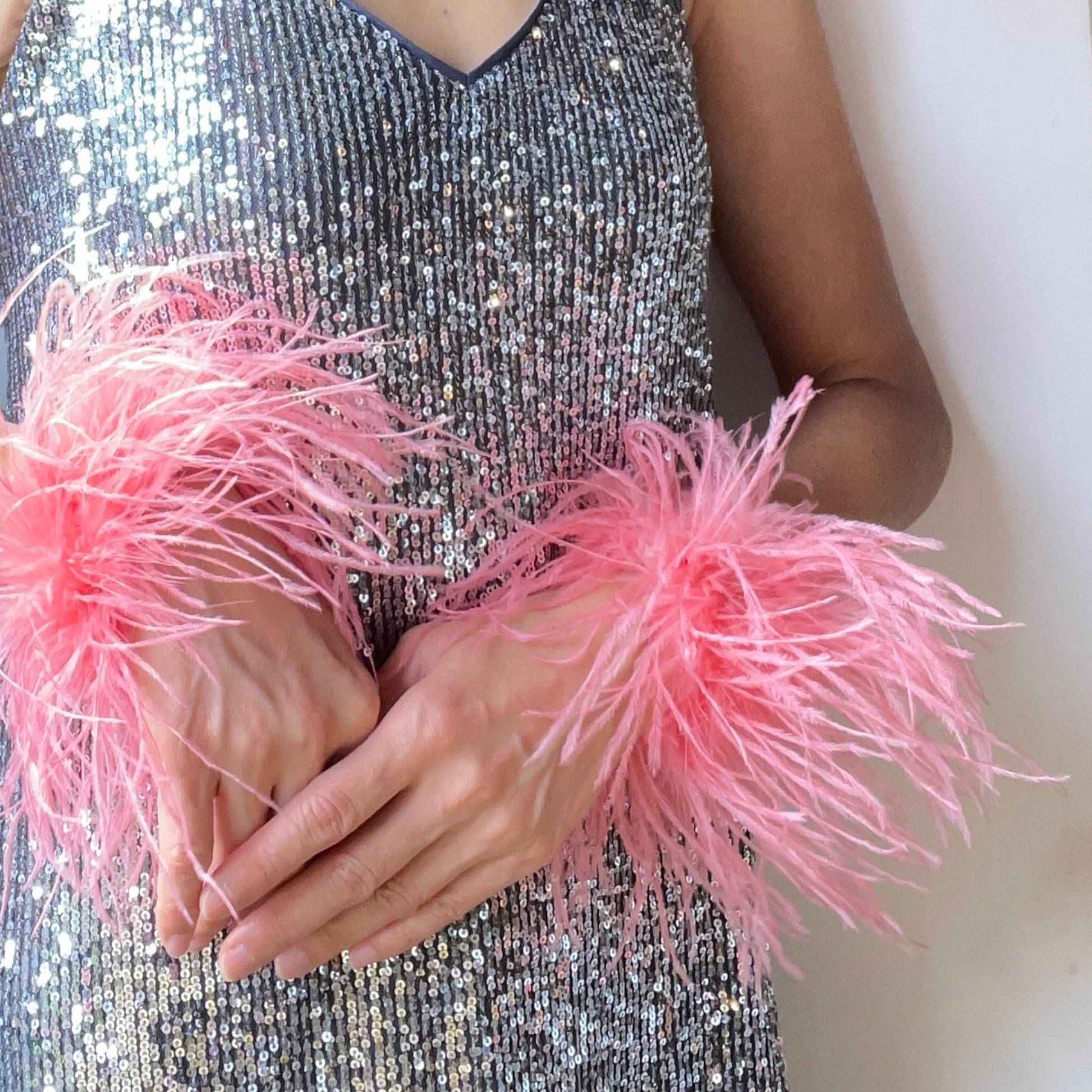 Person wearing a silver sequin dress with pink feather cuffs