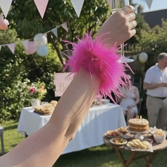 Video of a lady wearing a pink colored feather cuff at a sunny outdoors birthday party