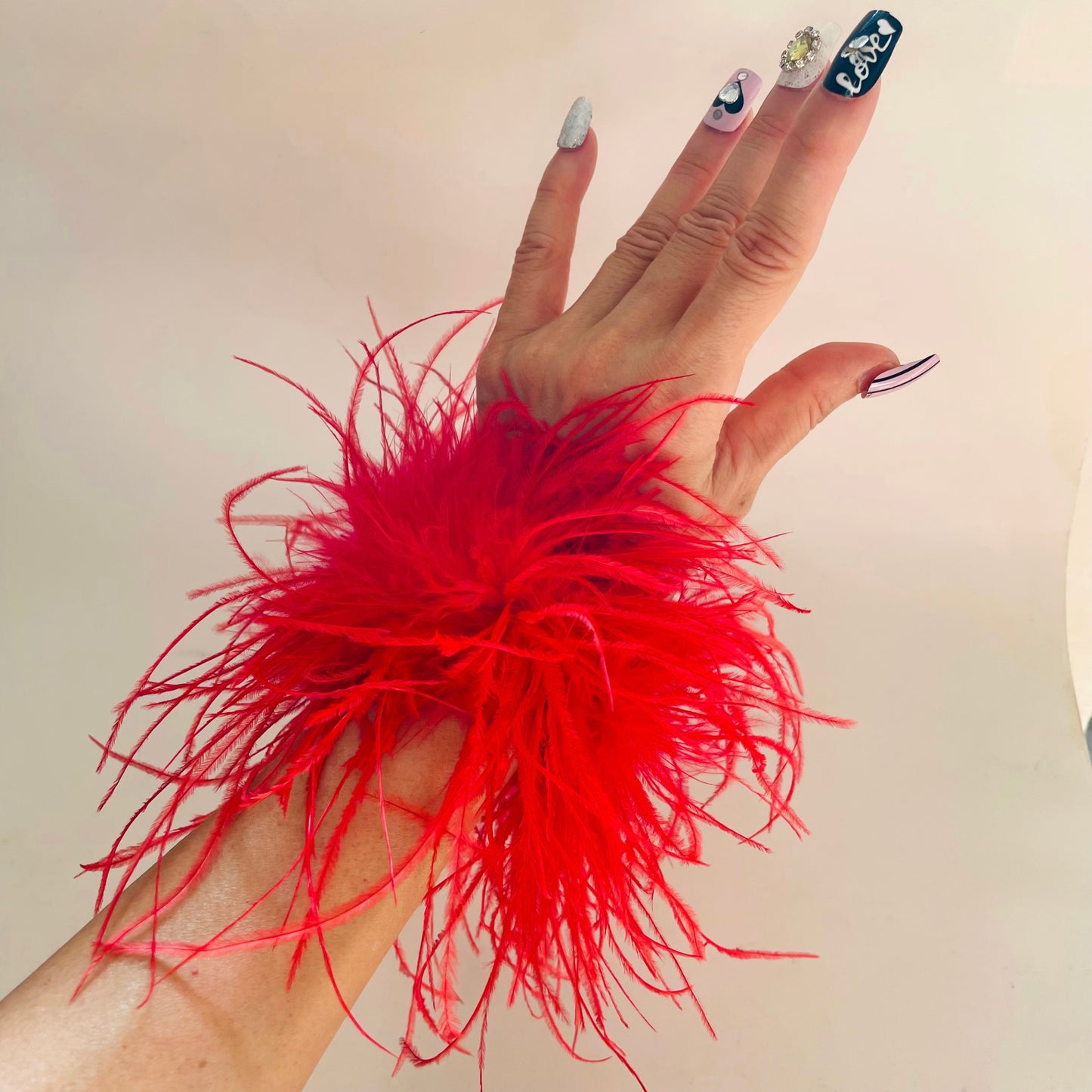 Hand wearing a red feather cuff accessory against a neutral background