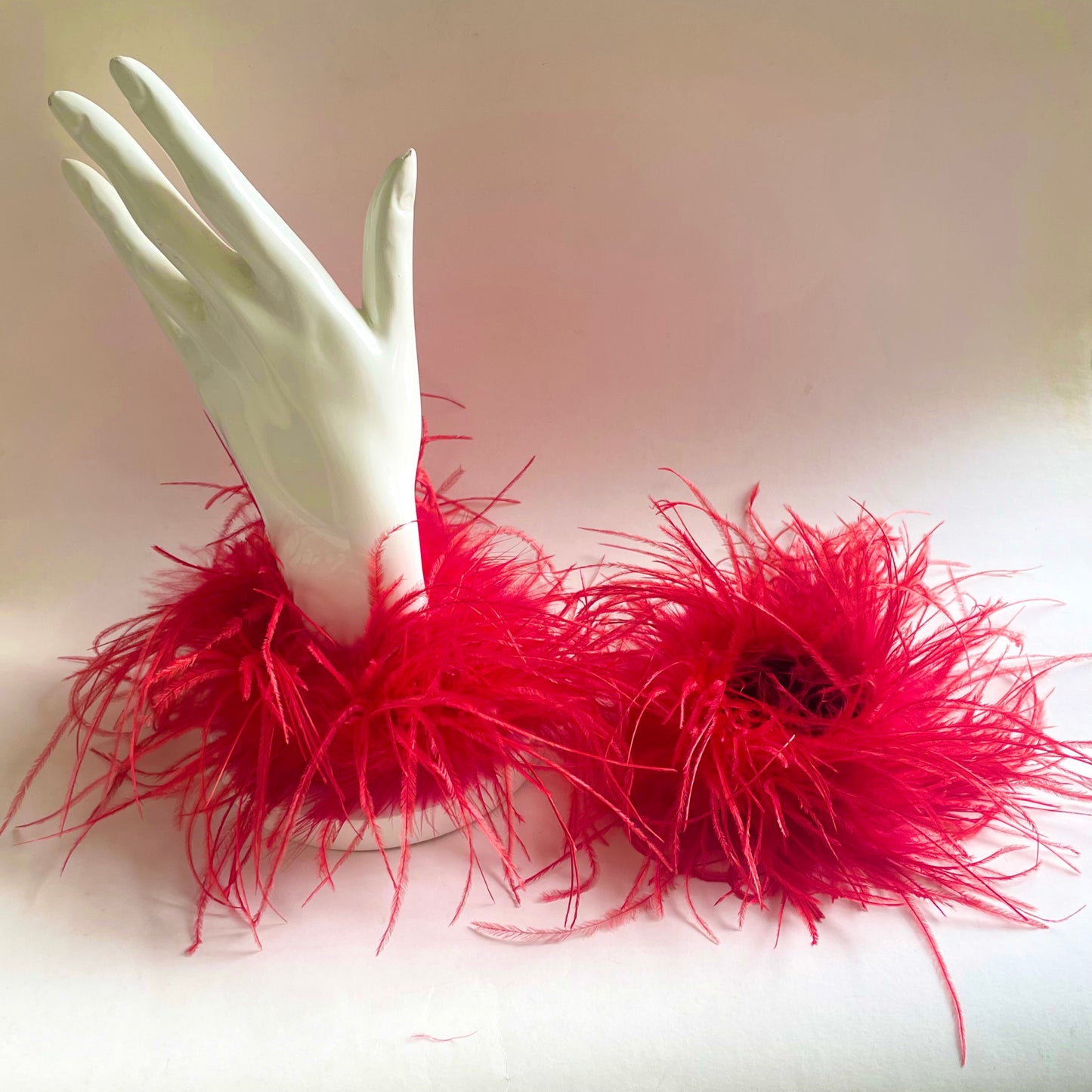 A pair of red feather cuff bracelet on a white mannequin hand placed against a white background