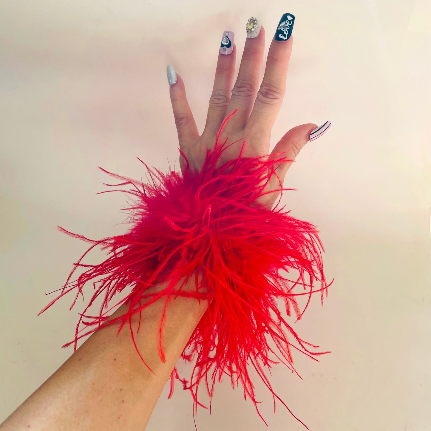 Hand wearing a red feather cuff bracelet against a plain background
