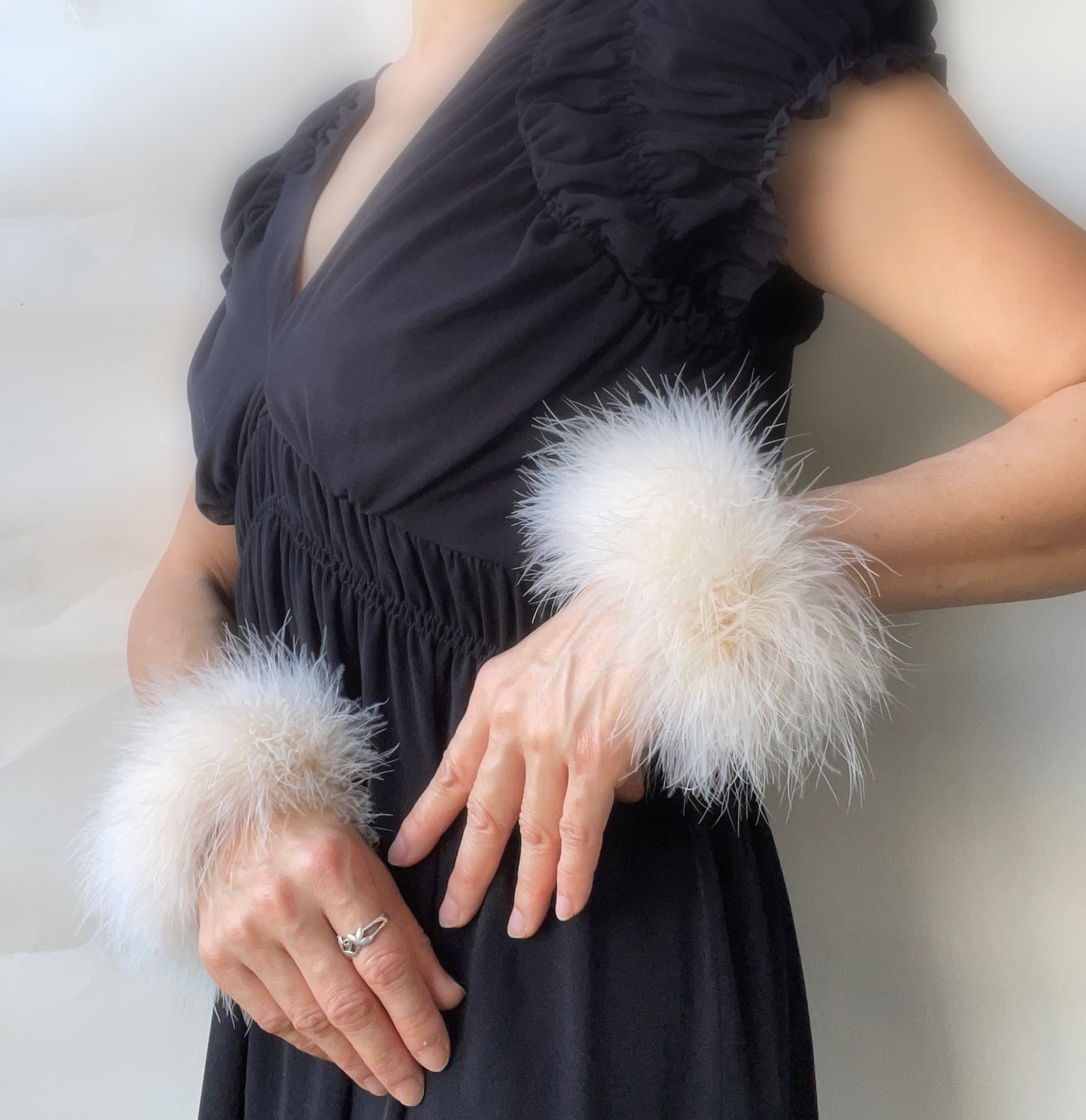 Person wearing a black dress with white marabou feather cuff accessories on a plain background
