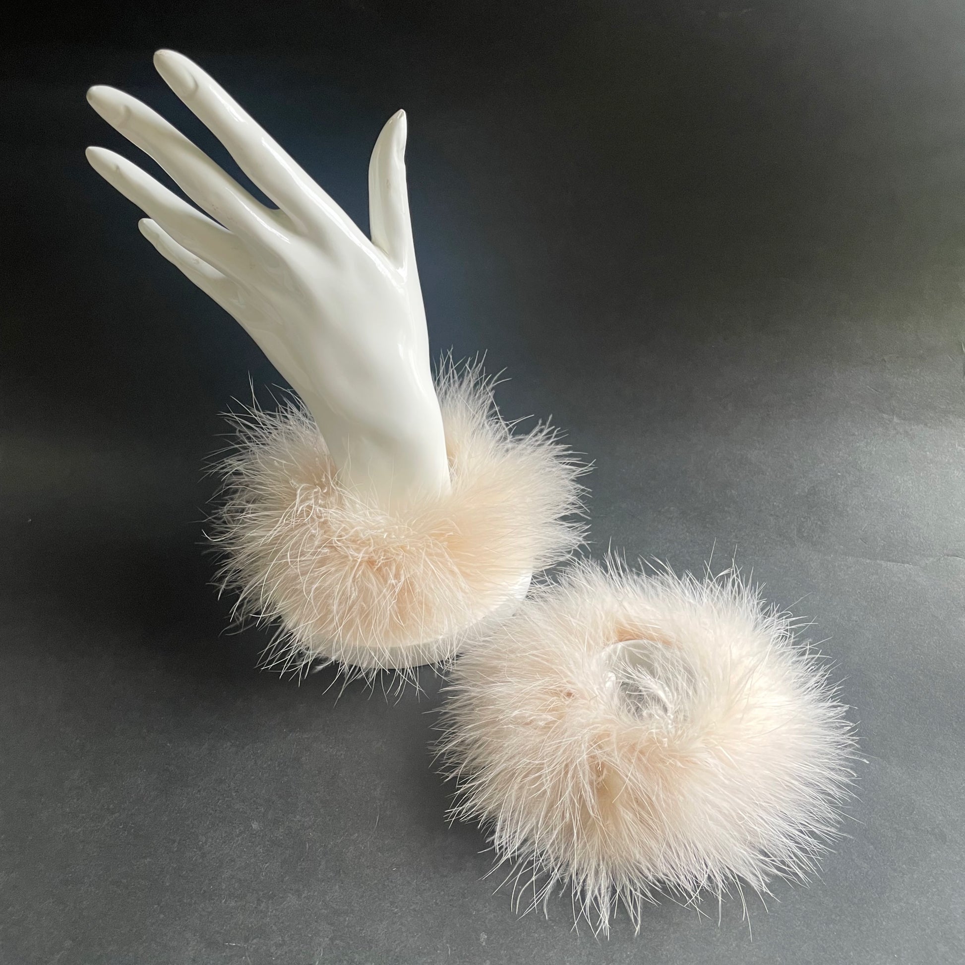 White mannequin hand with fluffy white marabou feather cuffs on a dark background