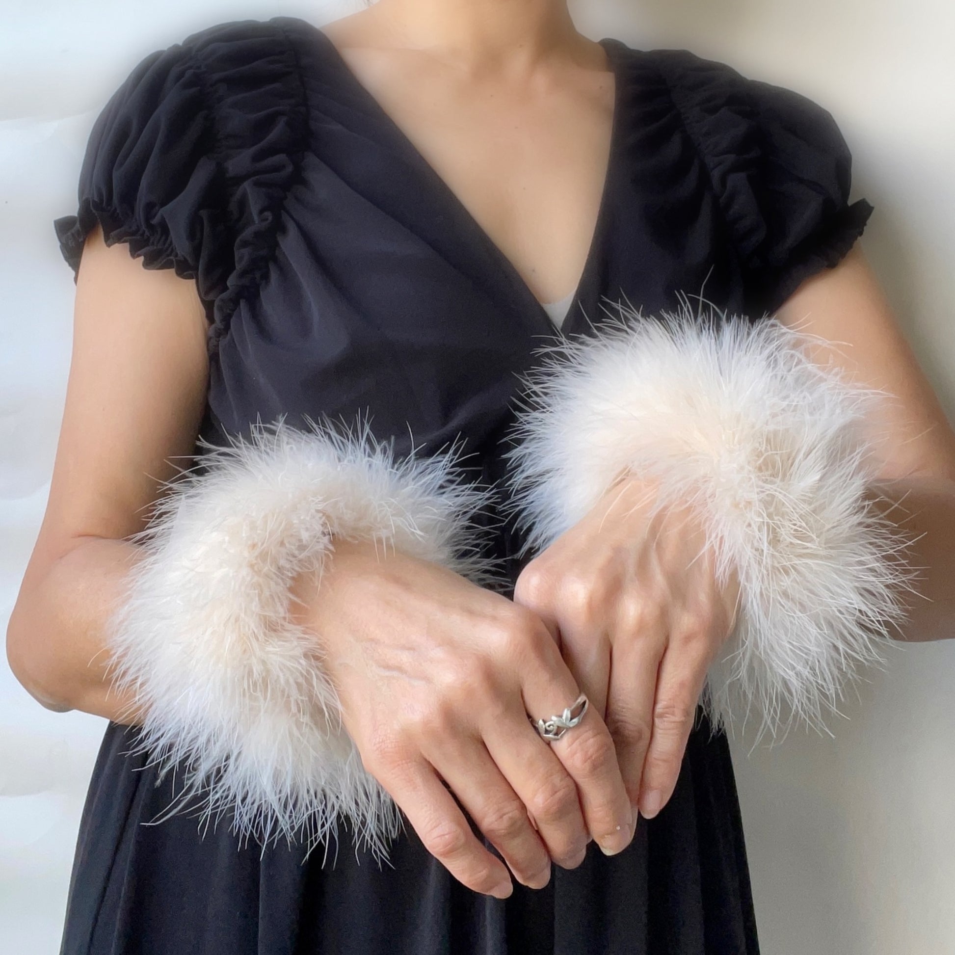 Person wearing a black dress with fluffy white marabou feather cuffs against a neutral background