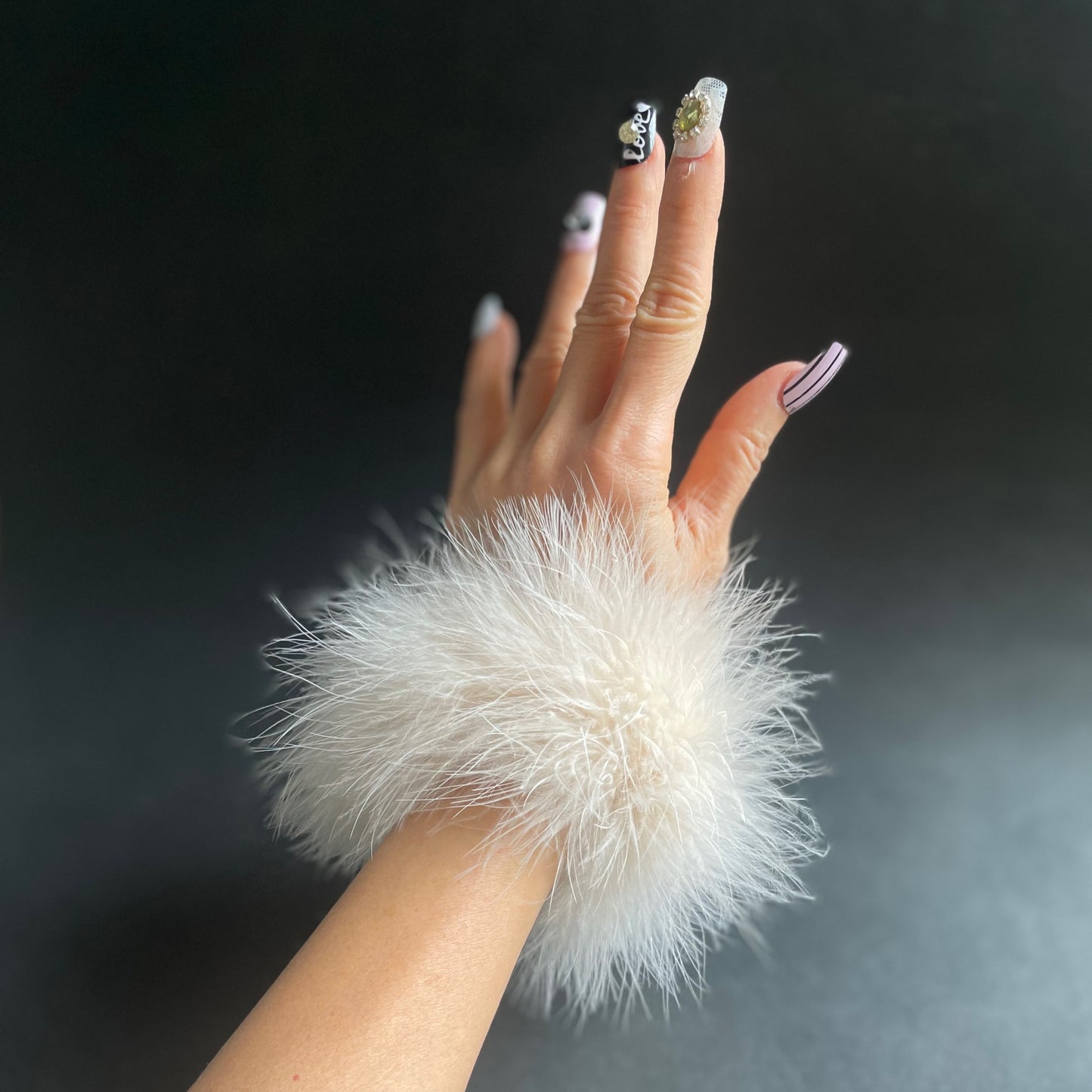 Hand wearing a fluffy white marabou feather cuff bracelet accessory against a dark background